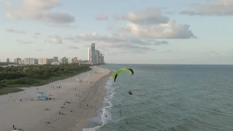 Aerial follows dynamic paramotor flight over sandy urban Miami Beach 動画素材 167985827