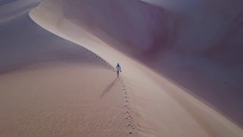 Aerial footage of a woman walking on a sand dune during sunrise. Stock Footage