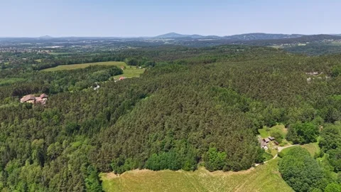 Aerial forest corridor over patchwork fields, scattered villages, distant hills Stock Footage 342355448
