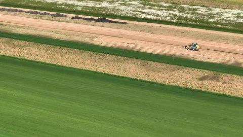 AERIAL: Forklift drives along a patch of dry soil running alongside a sod field. Stock Footage 268766082