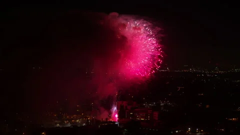 Aerial Forward Pink Sparks Of Exploding Fireworks In Illuminated City - Los Stock Footage 169490023
