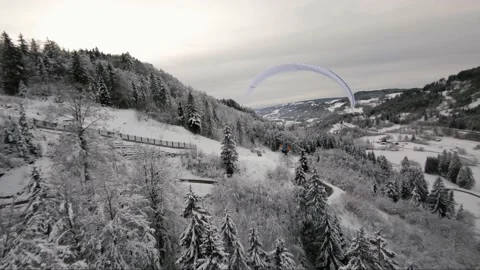 Aerial fpv shot of winter snowscape surrounding active paraglider flying Stock Footage 149190827