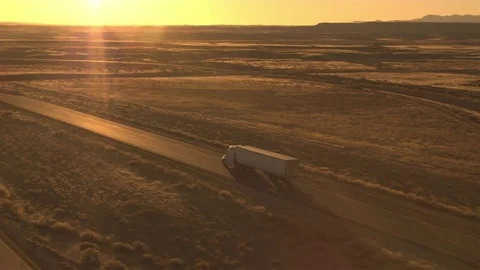 AERIAL Freight semi truck shipping goods across the vast plain wilderness in USA Stock Footage