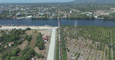 Aerial:  freight train crosses a river bridge between town and palm plantation Stock Footage 334909329