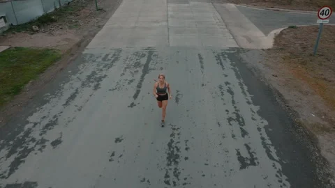 Aerial front view of female runner approaching sidewalk beside wooden fence Stock Footage 339621273