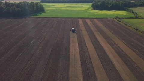 Aerial Front View of a Tractor Among Soil Strips with Green Fields Beyond Stock Footage 348787745