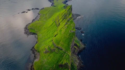 Aerial green island with a dramatic steep cliff jutting into the deep blue ocean Stock Footage 339780715