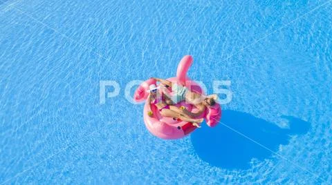 AERIAL: Guy and girl relaxing, sipping cocktails on fun flamingo floatie in pool Stock Photos