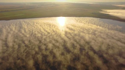AERIAL: A huge lake under a layer of thick fog at dawn. Bright morning sun Stock Footage 82471273