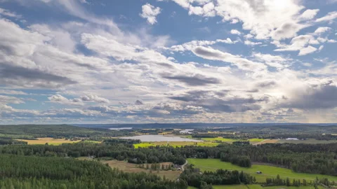 Aerial hyperlapse of cloudscape drifting over lush Swedish countryside, tilt-up Stock Footage 300381664