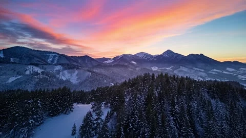 Aerial hyperlapse over winter mountain forest and snowy peaks under colorful Video stock 322671071