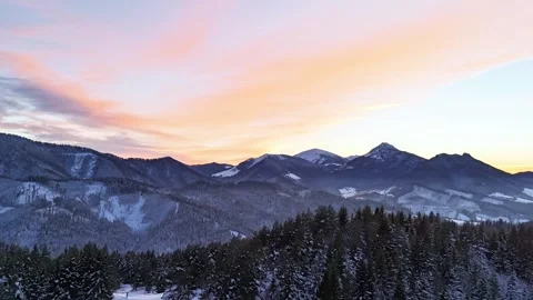 Aerial hyperlapse over winter mountain forest and snowy peaks under colorful Stock Footage 323384931