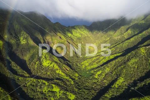 Aerial image of the lush mountains surrounding Oahu with a rainbow in the foregr Stock Photos