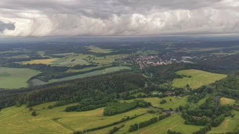 Aerial landscape view of patchwork fields and village beneath dramatic storm Stock Footage 347912960