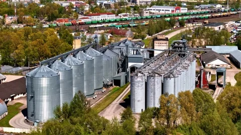 Aerial of large industrial grain elevator complex with metal silos and nearby Stock Footage 333158776