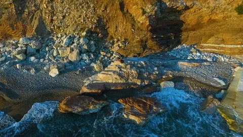 Aerial, lonely young man playing guitar sitting on a coastal rock Stock Footage 112728043