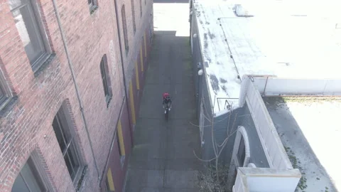 Aerial Long View of Bicycle Delivery Person Riding Down Alley Stock Footage 208777897