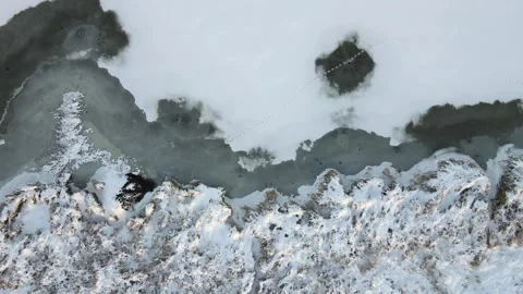 Aerial looking down and rising above a snow covered lake and shore with tracks Stock Footage 289028553