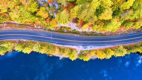 Aerial looking down on road between blue water lake and rocky forest in fall Stock Photos