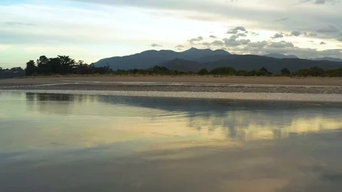 Aerial low above water surface mirroing the colors of sunset and Takaka Hill Video stock 126971027