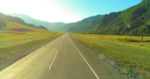 Aerial low air flight over mountain road and meadow at sunny summer morning. Stock Footage 106923799
