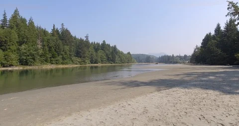 Aerial low fast push over river with trees, mountains and small settlement Stock Footage 86297232