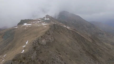 Aerial low flight at peak of the mountain into the clouds while snowing Stock Footage 215915628