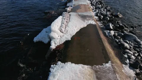 Aerial low flight: Waves hitting pier covered in ice in winter slow motion Stock Footage 151882895