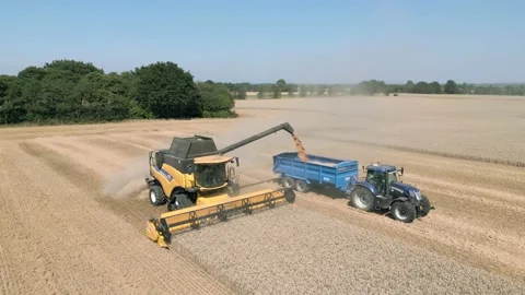Aerial low level view clip tracking a combine harvester harvesting and unloading Stock Footage 205330845