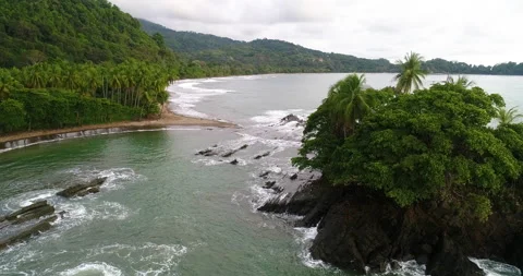Aerial Low Over Cloudy Volcanic Coastline Surf And Lush Jungle With Palm Trees Video stock 135285337