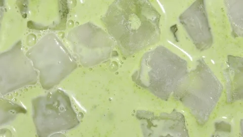 Aerial macro view of ice cubes floating in creamy matcha tea, vibrant green Stock Footage 318285751