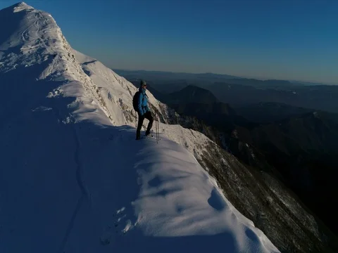 Aerial - Male climber standing on top of snowy ridge at sunset Stock Footage