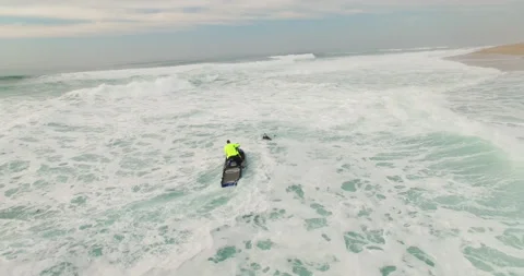 Aerial of man on jet ski pulling out skilful surfer from ocean water in Nazare Stock Footage 160499897
