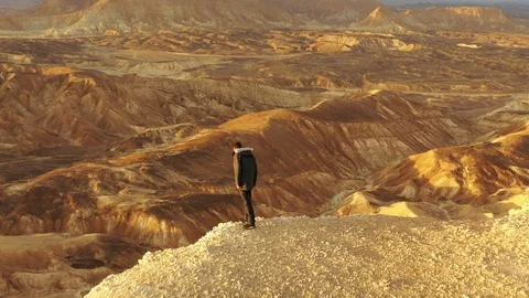 Aerial of A Man Looking Down the ide of a Cliff in the Desert in Negev Desert, Stock Footage 109191444