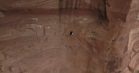 Aerial of man rappelling/abseiling down through an enormous sandstone cave Stock Footage 111406780