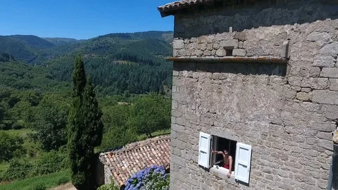 Aerial of a man waving at the window in a mountain cottage during summer Stock Footage 89781973