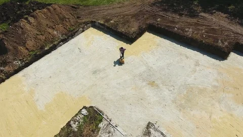 Aerial of man working with plate compactor in foundation pit of new house Stock Footage 107986976