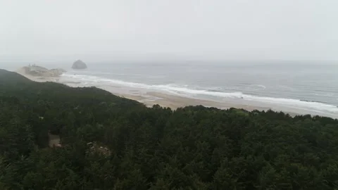 Aerial at McPhillips beach, Oregon over pine forest and rock island in low fog Stock Footage 219345993