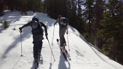 Aerial medium-close push over two backcountry skiers skinning up a hill Stock Footage 209988852