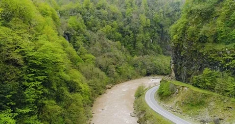 Aerial: Motion view of dirty river and a curving road through mountains 4K Stock-Footage 87912840