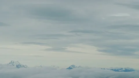 Aerial of Mountain peaks in lower frame, pastel clouds above Stock Footage 154987939