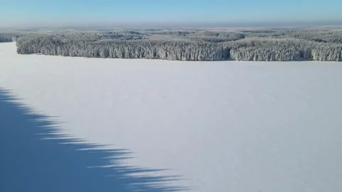 Aerial moving forward over a large snow-covered lake towards a vast snowy forest Stock Footage 247662177