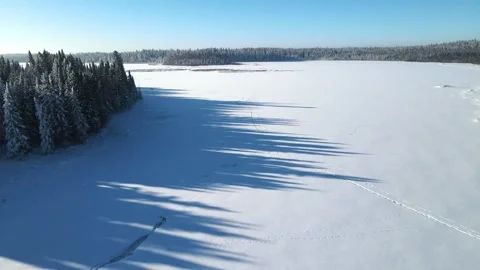 Aerial moving forward over a snow-covered lake that is surrounded by a forest Stock Footage 245999465