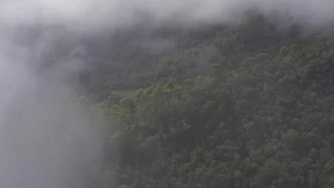 Aerial moving through thin white cloud to reveal calming view of green mountain Stock Footage 284247574