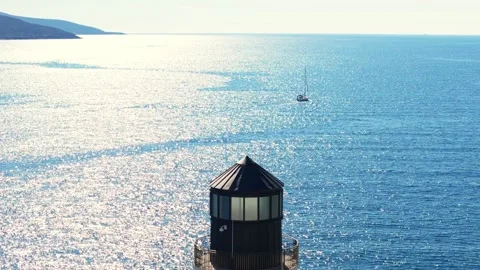 Aerial of octagonal lighthouse lantern and balcony by sunlit sea Stock Footage 327013525