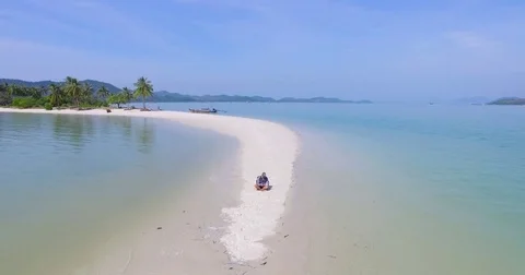 Aerial: One man siting on the edge of the beach and runs the drone. Stock Footage 72286427
