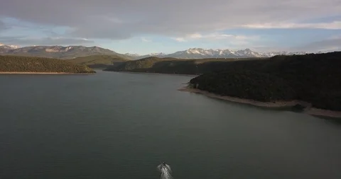 Aerial: one tiny boat cruises along on a beautiful mountain lake Stock Footage 99571406