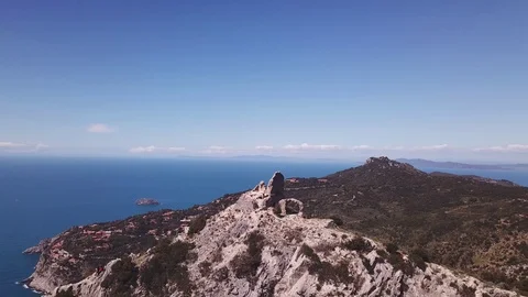 Aerial orbit around a peak with Tower on a cliff by the sea, some trekkers on it Stock Footage 107180958
