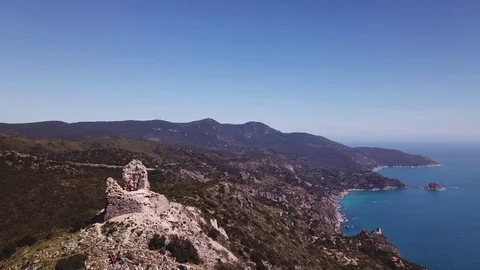 Aerial orbit around a peak with Tower on a cliff by the sea, some trekkers on it Stock Footage 107181089