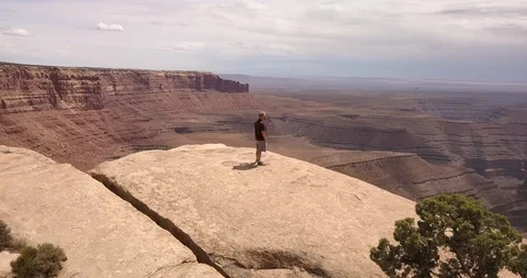 Aerial: orbit of man standing triumphantly on desert cliff near monument valley Stock Footage 99451925